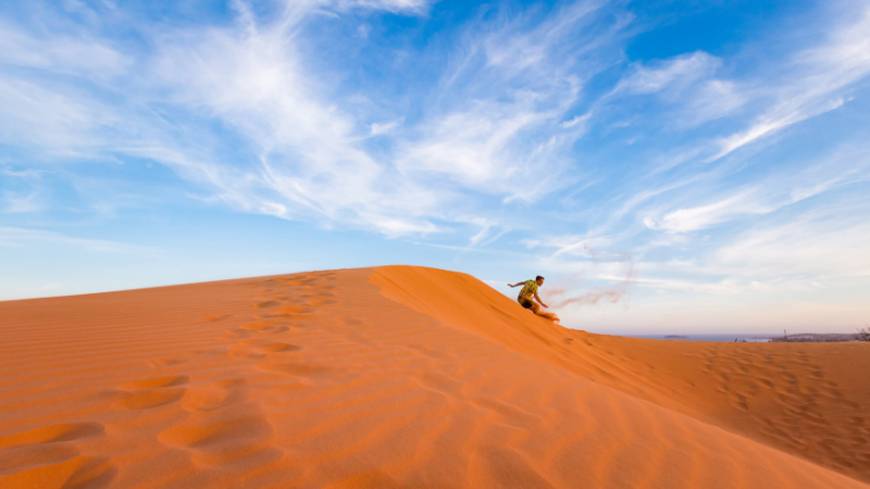 Adventure Vietnam Travel sandboarding on golden dunes in Mui Ne under blue skies