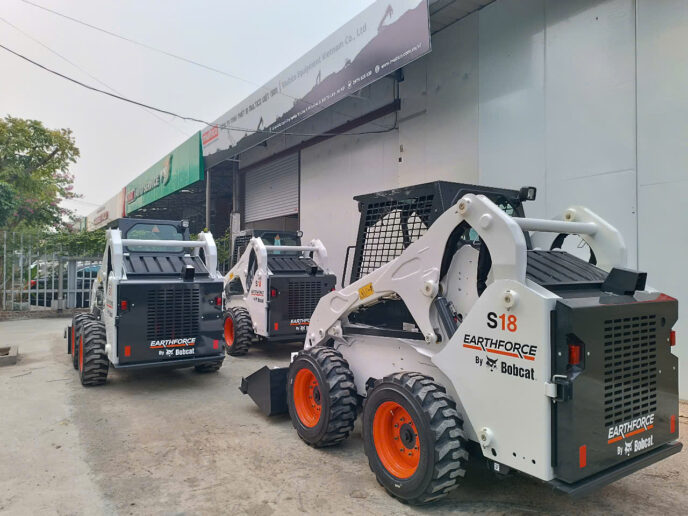 Giới Thiệu Về Máy Xúc Trượt Bobcat S18 Hình ảnh giới thiệu chiếc máy xúc trượt Bobcat S18 đang có sẵn tại kho của Công ty TNHH Thiết Bị Multico Việt Nam. Trong ảnh, chiếc Bobcat S18 nổi bật với thiết kế hiện đại, màu trắng cam đặc trưng, được trưng bày trong không gian kho bãi sạch sẽ và chuyên nghiệp của Multico.